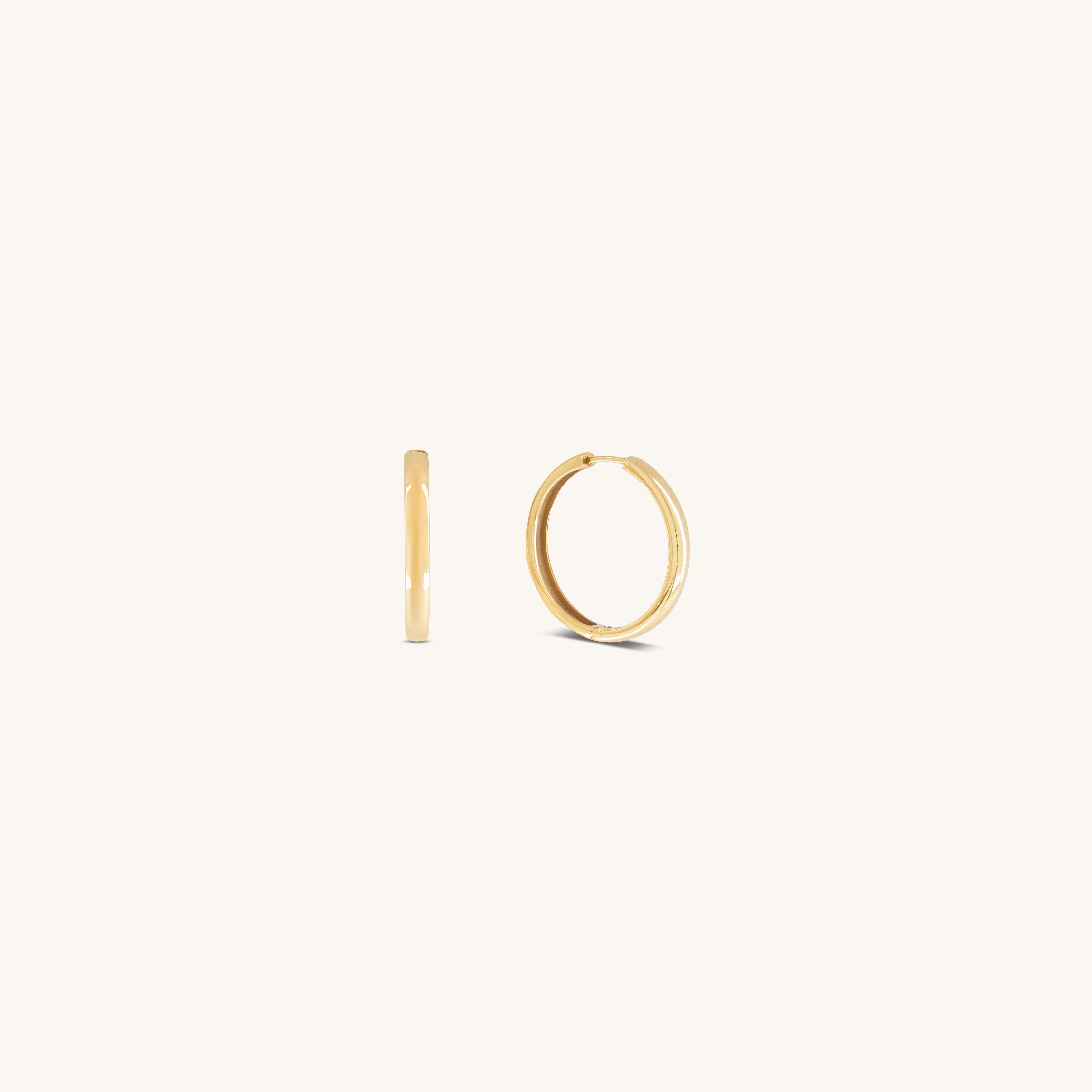 Two small, simple Gertrude Hoops by Glasâje are shown on a plain, light background—crafted in 9ct solid gold with a 23mm diameter. One earring is displayed from the side and the other from the front.