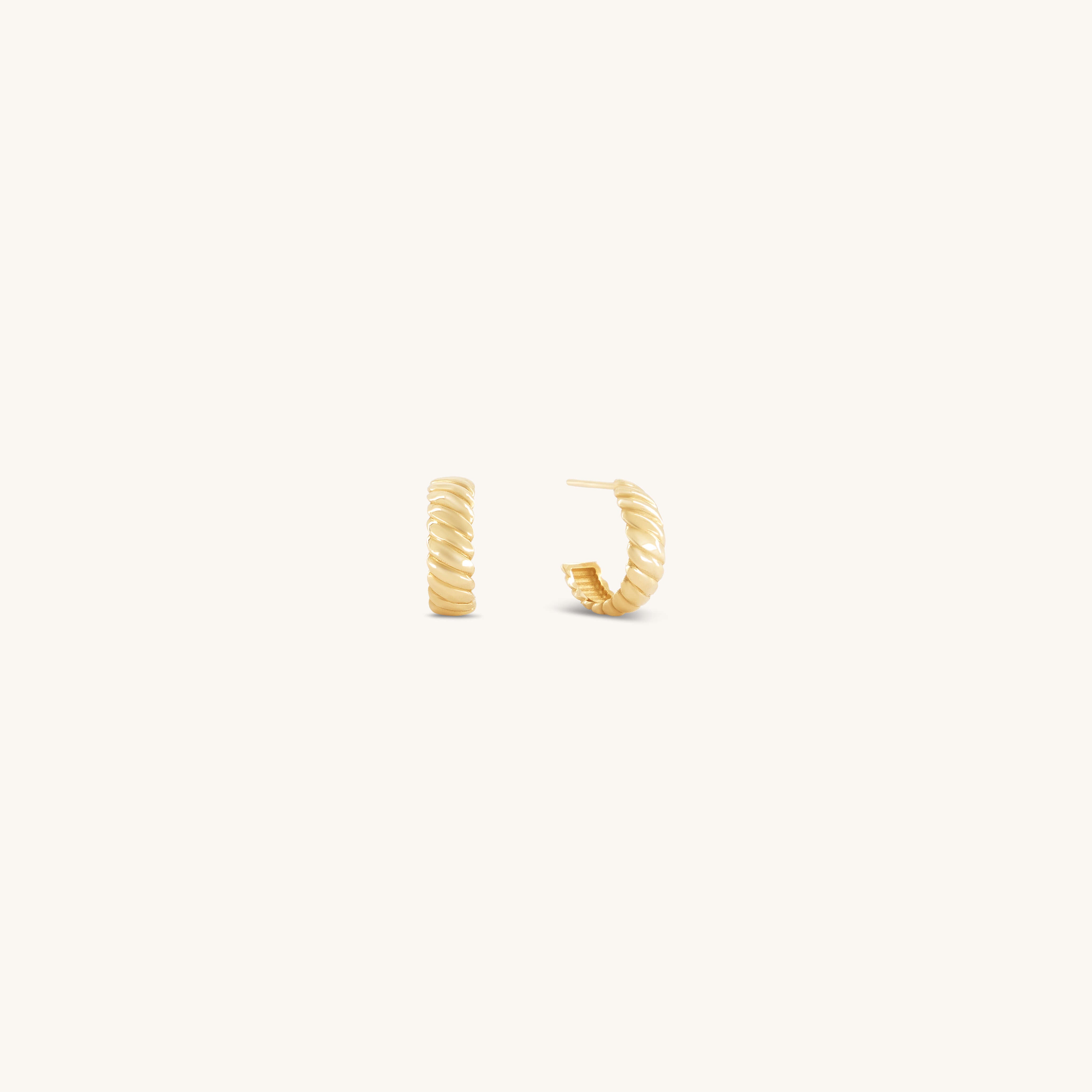 Gold hoop earrings with a twisted design are set against a white background. They convey a sense of elegance and simplicity, highlighting their textured surface.