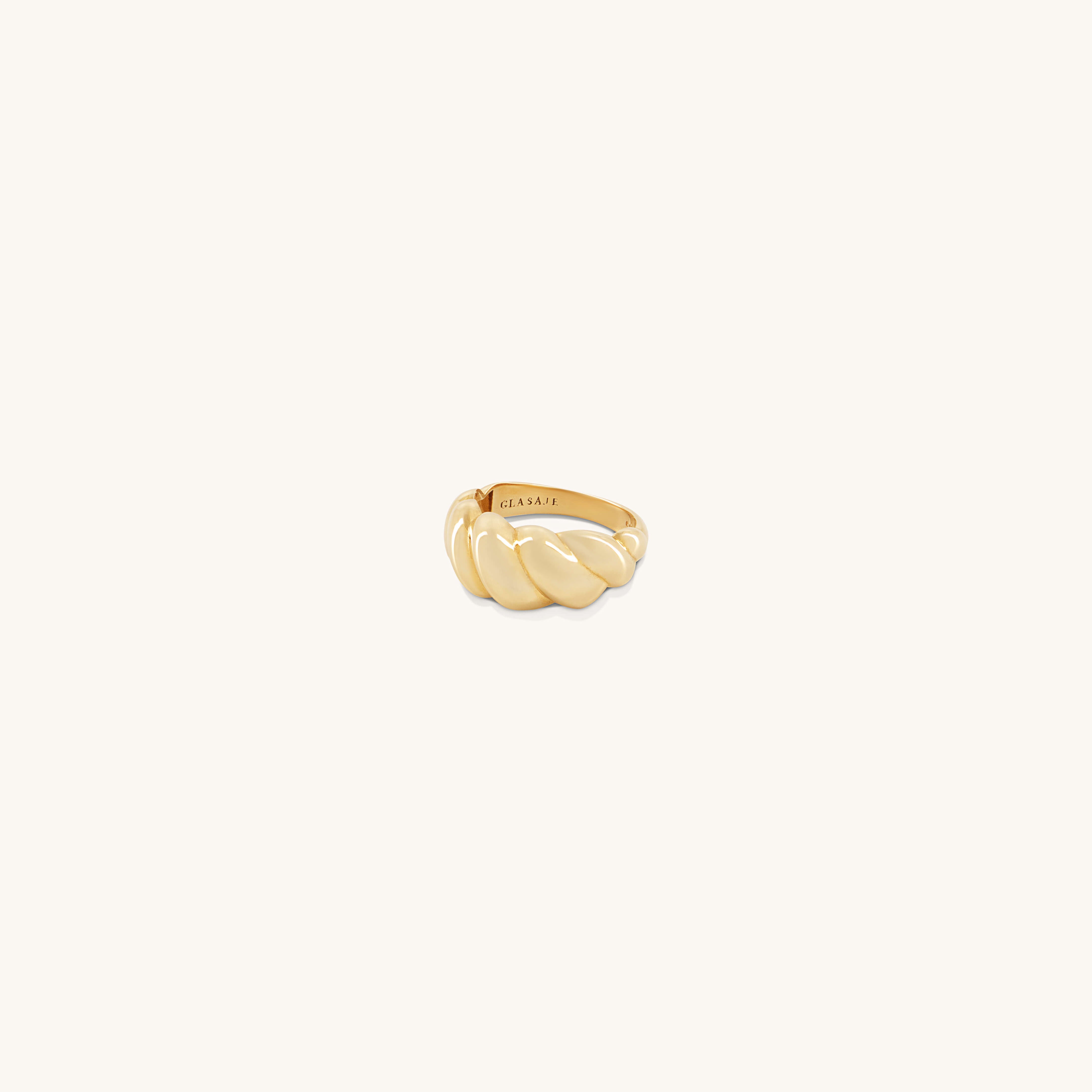 A gold, twisted croissant-shaped Lune Ring with a polished finish is displayed on a plain background. The inner band features the brand name Glasâje engraved.