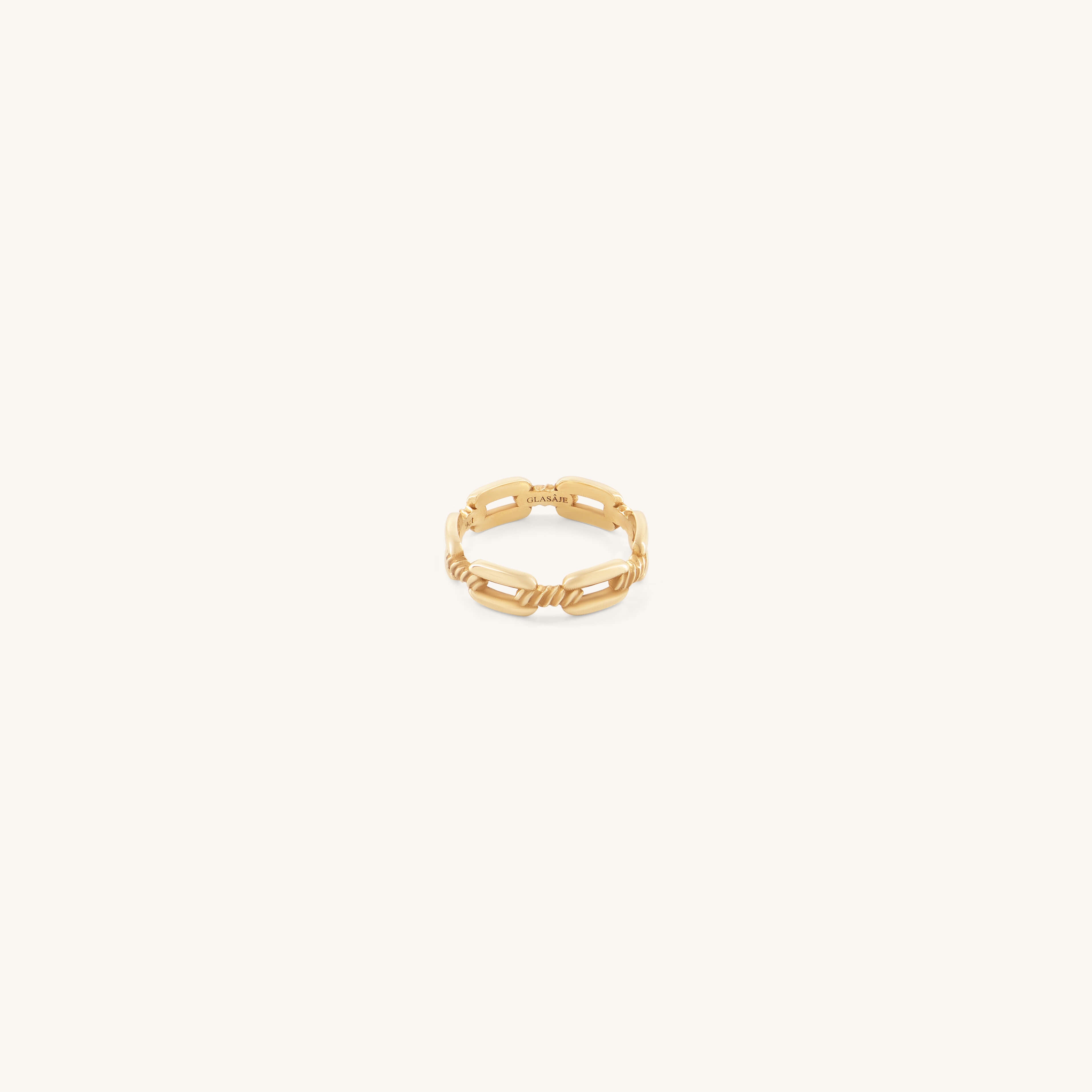A delicate gold ring with a chain-link design on a soft cream background. The ring's intertwined pattern conveys elegance and modern style.