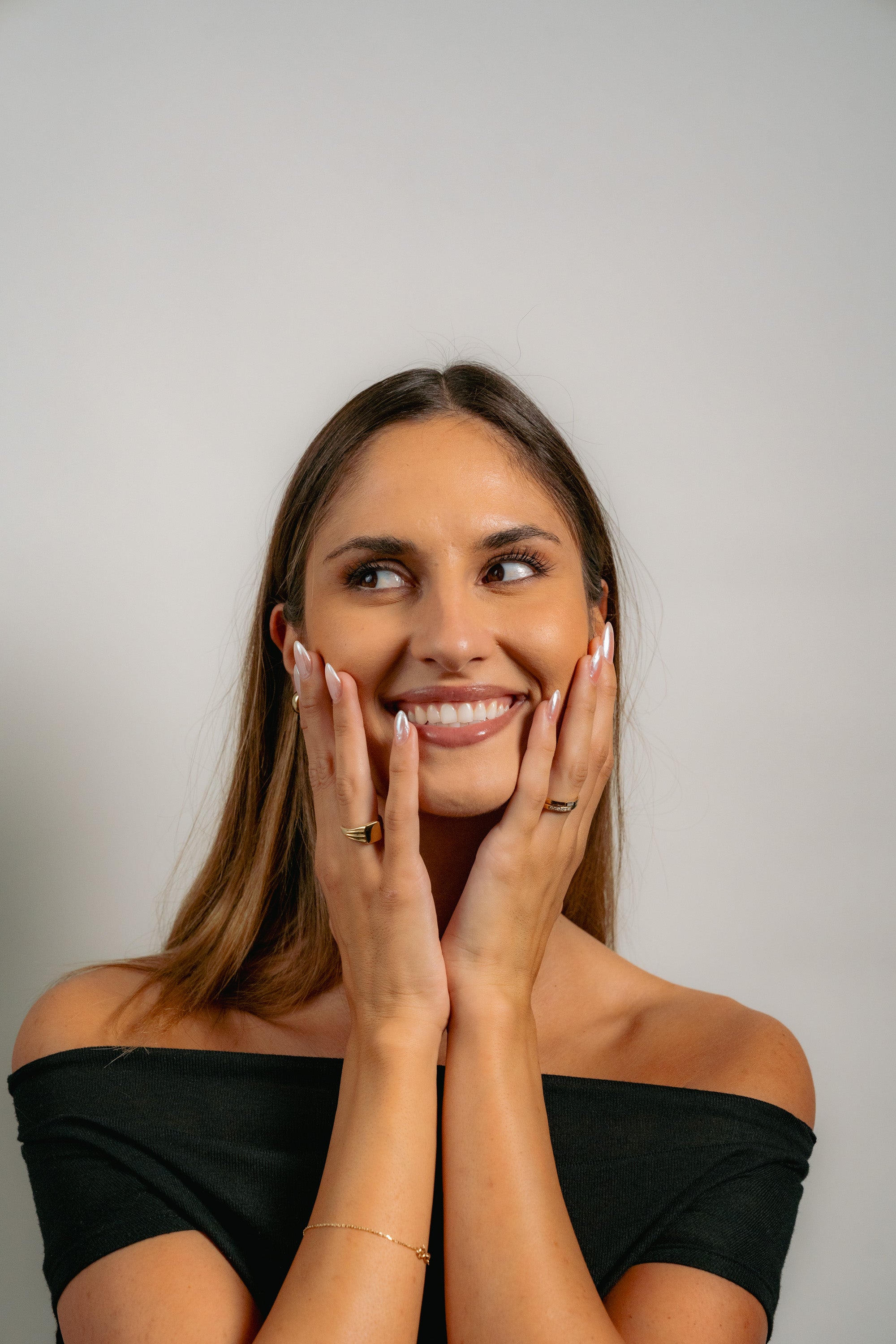 Woman with a bright smile and hands on face against a plain background